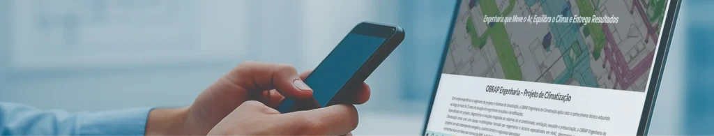 Mãos humanas segurando smartphone diante de notebook aberto com projeto técnico HVAC na tela, em ambiente corporativo moderno e iluminado, representando contato profissional da OBRAP Engenharia de Climatização